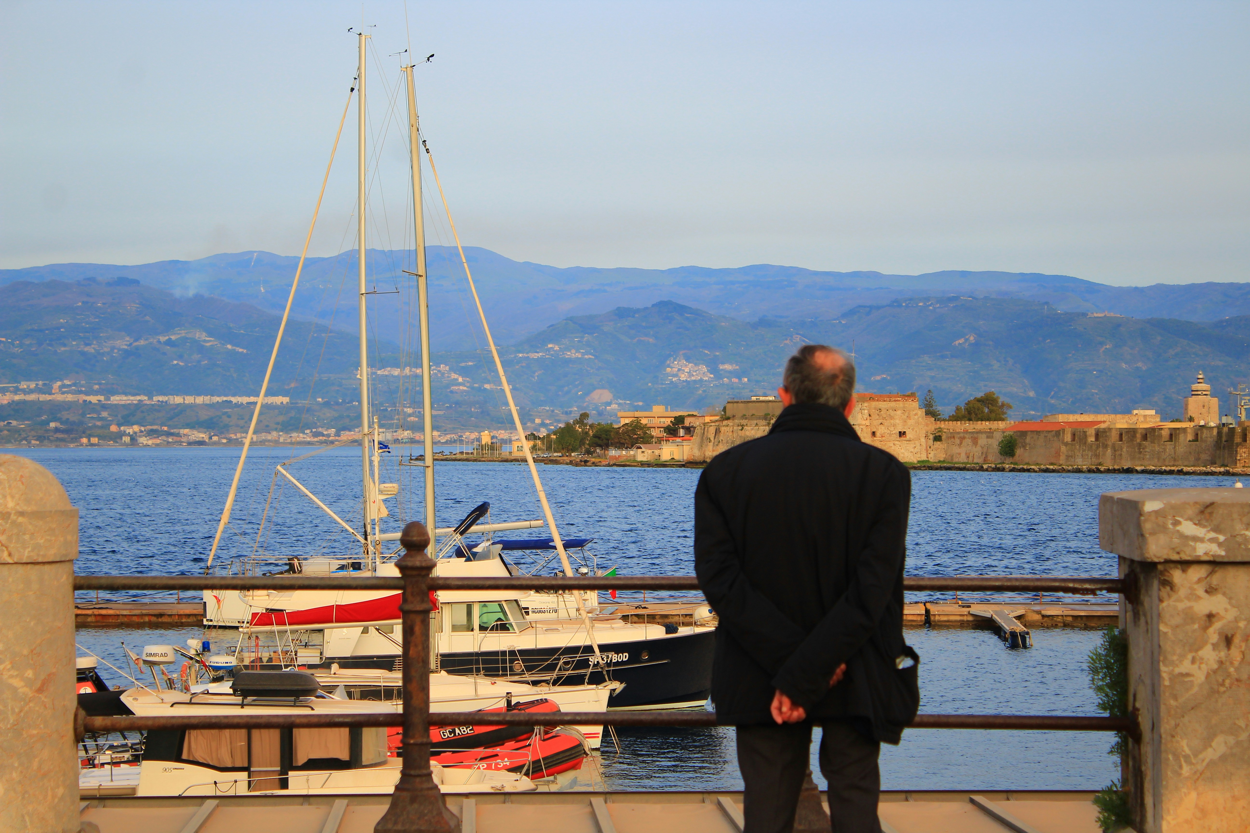 a man standing on a dock looking at a sailboat