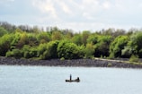 Family enjoying fishing from a boat on calm waters surrounded by lush trees.