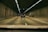 Vehicles drive through a dimly lit tunnel with tiled walls and overhead lights. The scene captures a straight road with a yellow line on the left and white dashed lines dividing lanes. Multiple vehicles are moving forward in an orderly manner.