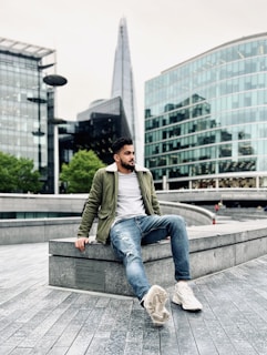 A man sitting relaxed on a bench wearing ripped jeans and sneakers, smiling naturally.