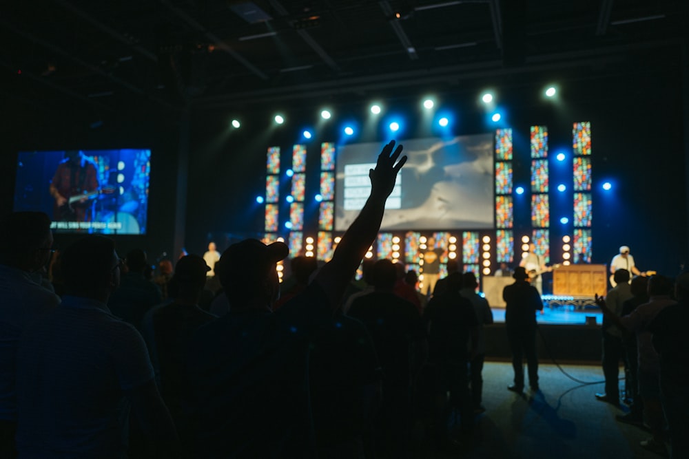 a crowd of people in a room with a stage and a large screen