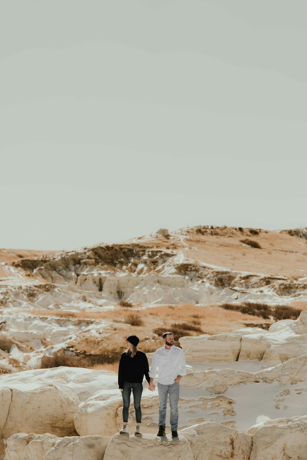 a man and woman standing on a rocky hillside with a rainbow in the background