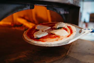 A chef sliding a pizza into the blazing wood-fired oven with a wooden peel.