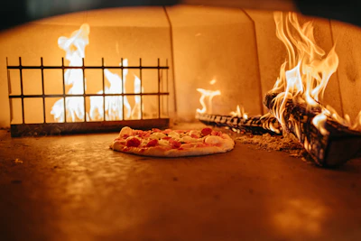 A chef placing a pizza into a traditional stone oven with flames glowing inside.