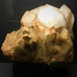 A cluster of large, translucent quartz crystals with a light brown and white color palette. The crystals have various sizes and are arranged in an irregular formation. The surface is rough with visible mineral deposits, showcasing the natural beauty of the mineral.