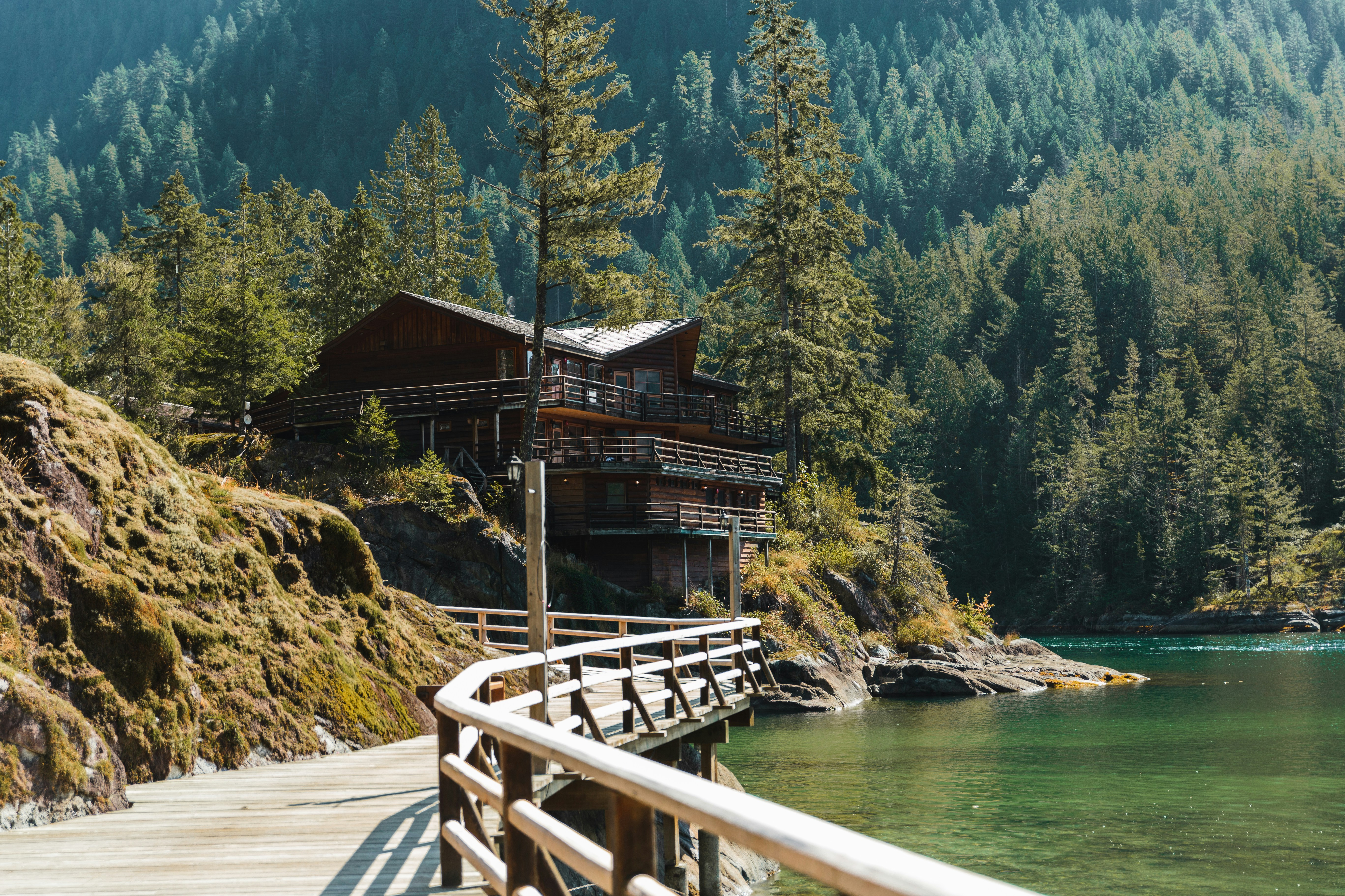 a wooden building on a dock over water with trees and mountains in the background