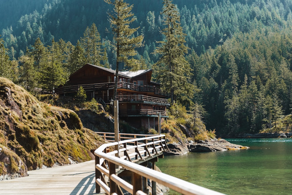 a wooden building on a dock over water with trees and mountains in the background