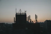 Technician inspecting telecommunications infrastructure on a rooftop at sunset.