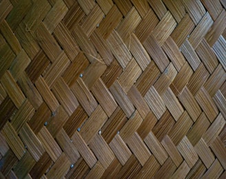 A close-up view of a woven bamboo pattern consisting of interlaced strips forming a herringbone design. The texture is detailed, showcasing the natural variations in the bamboo fibers.