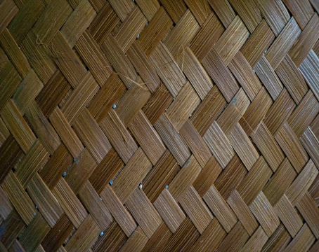 A close-up view of a woven bamboo pattern consisting of interlaced strips forming a herringbone design. The texture is detailed, showcasing the natural variations in the bamboo fibers.