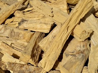 A pile of chopped wood pieces with rough, uneven textures. The wood appears dry and is mostly light brown in color, with visible grain patterns and some darker spots.