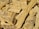 A pile of chopped wood pieces with rough, uneven textures. The wood appears dry and is mostly light brown in color, with visible grain patterns and some darker spots.