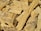 A pile of chopped wood pieces with rough, uneven textures. The wood appears dry and is mostly light brown in color, with visible grain patterns and some darker spots.
