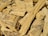 A pile of chopped wood pieces with rough, uneven textures. The wood appears dry and is mostly light brown in color, with visible grain patterns and some darker spots.
