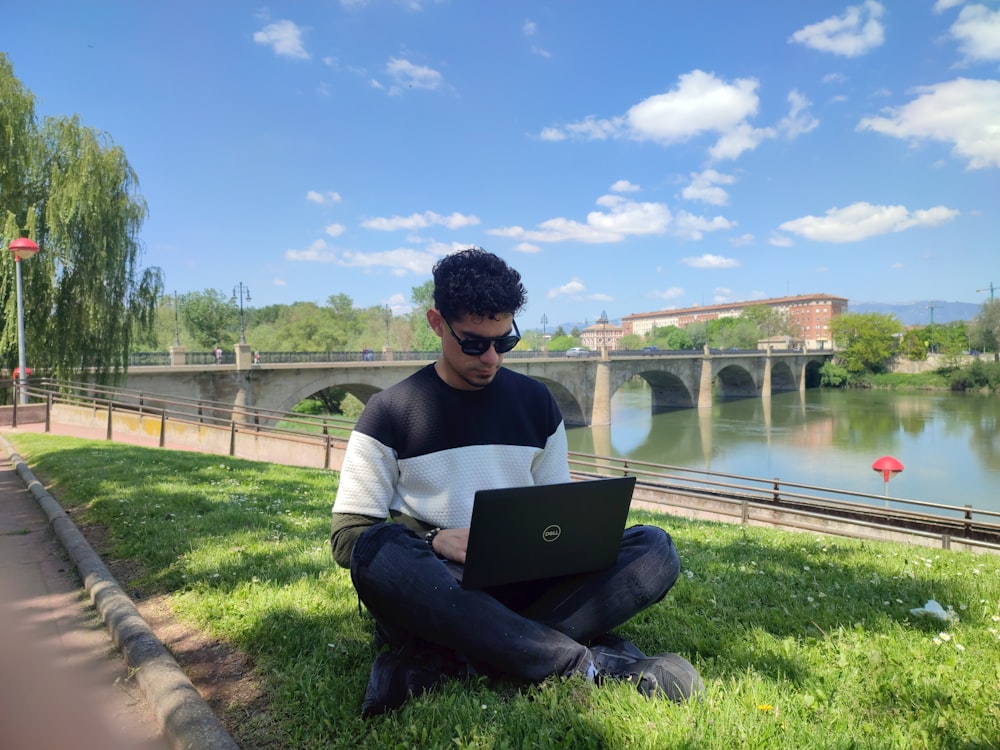 a man sitting on grass with a laptop