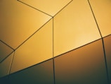 Close-up of a geometric pattern etched in soft gold on a muted ochre wall.