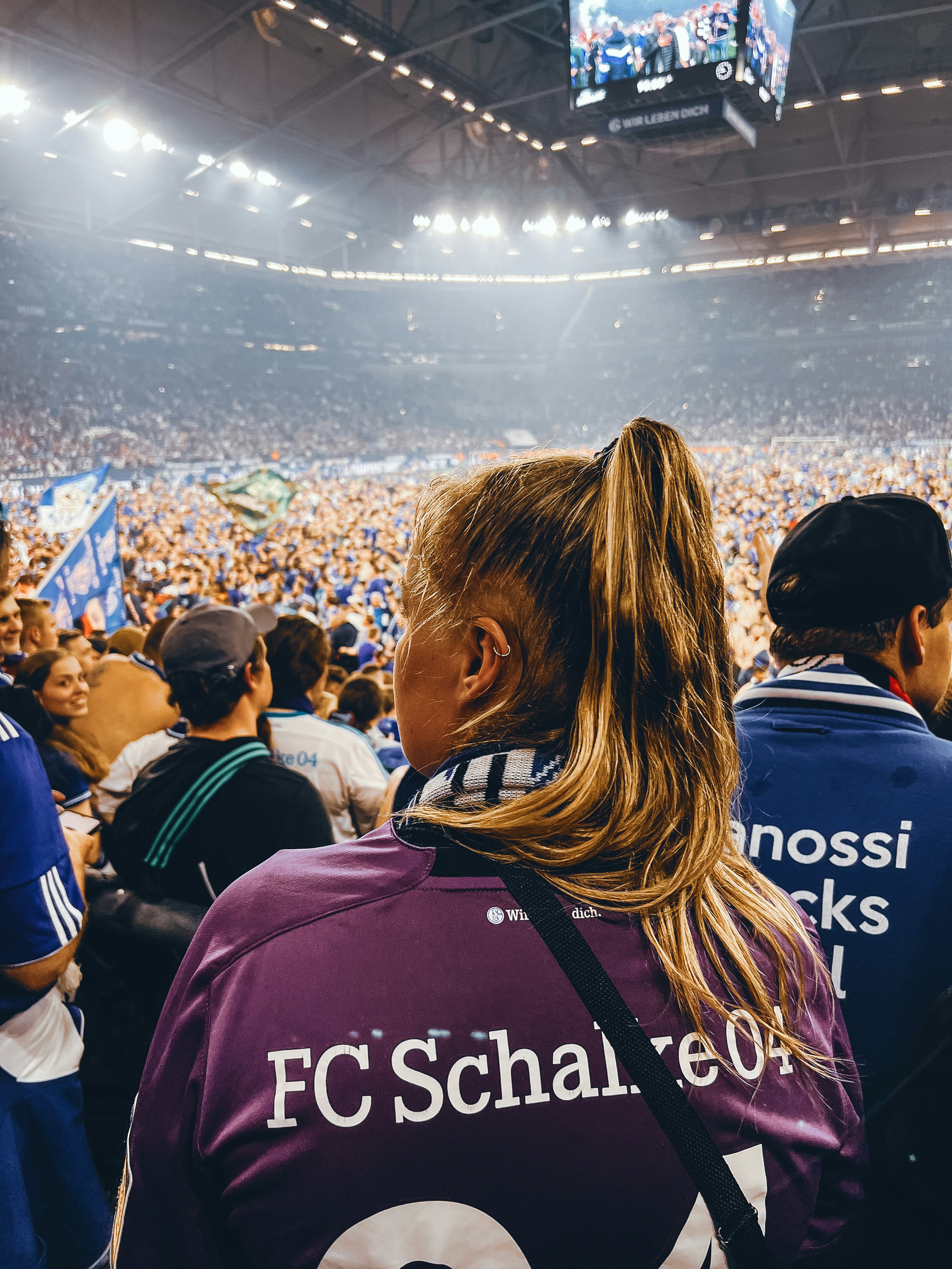 Sports fans wearing jerseys in dark stadium with colorful crowd lighting and team scarves