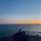 Couple relaxing on a terrace overlooking the sea during a warm sunset.