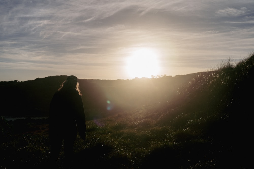 uma pessoa de pé em uma colina olhando para o sol