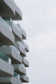 A series of wavy, modern balconies extending from a building against a light sky, each balcony featuring glass railings.
