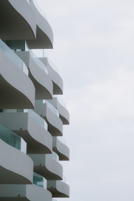 A series of wavy, modern balconies extending from a building against a light sky, each balcony featuring glass railings.