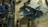 A detailed model airplane is surrounded by various painting supplies, including paints, brushes, and containers. The plane is a dark blue color with military-style markings and is resting on a textured surface.