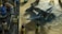 A detailed model airplane is surrounded by various painting supplies, including paints, brushes, and containers. The plane is a dark blue color with military-style markings and is resting on a textured surface.