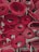 Several rolled-up red carpets are stacked closely together. The edges of the carpets fray slightly, and the rolls are tightly wound, showcasing different patterns and layers within the rolls.