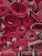 Several rolled-up red carpets are stacked closely together. The edges of the carpets fray slightly, and the rolls are tightly wound, showcasing different patterns and layers within the rolls.