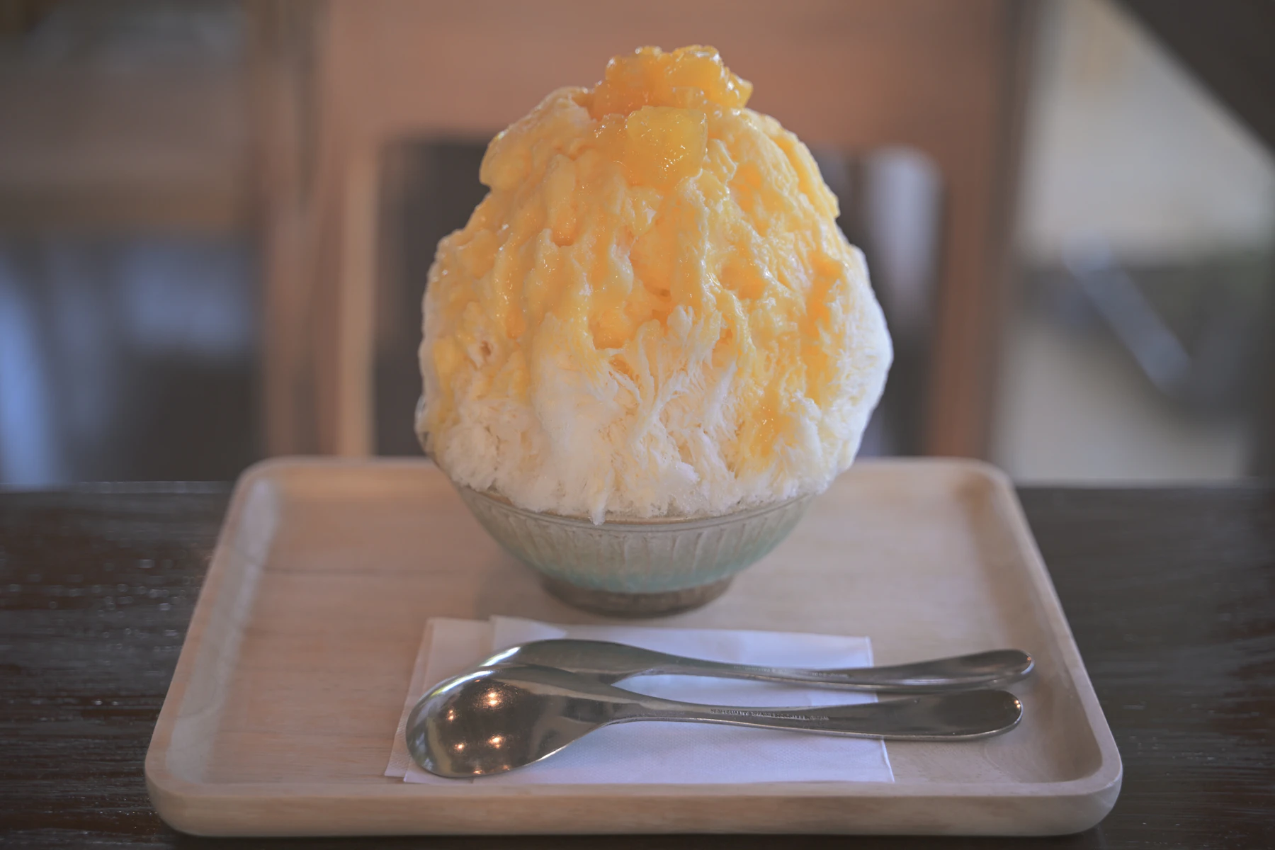 A tall mound of finely shaved ice soaked with mango syrup in a ceramic bowl on a wooden tray