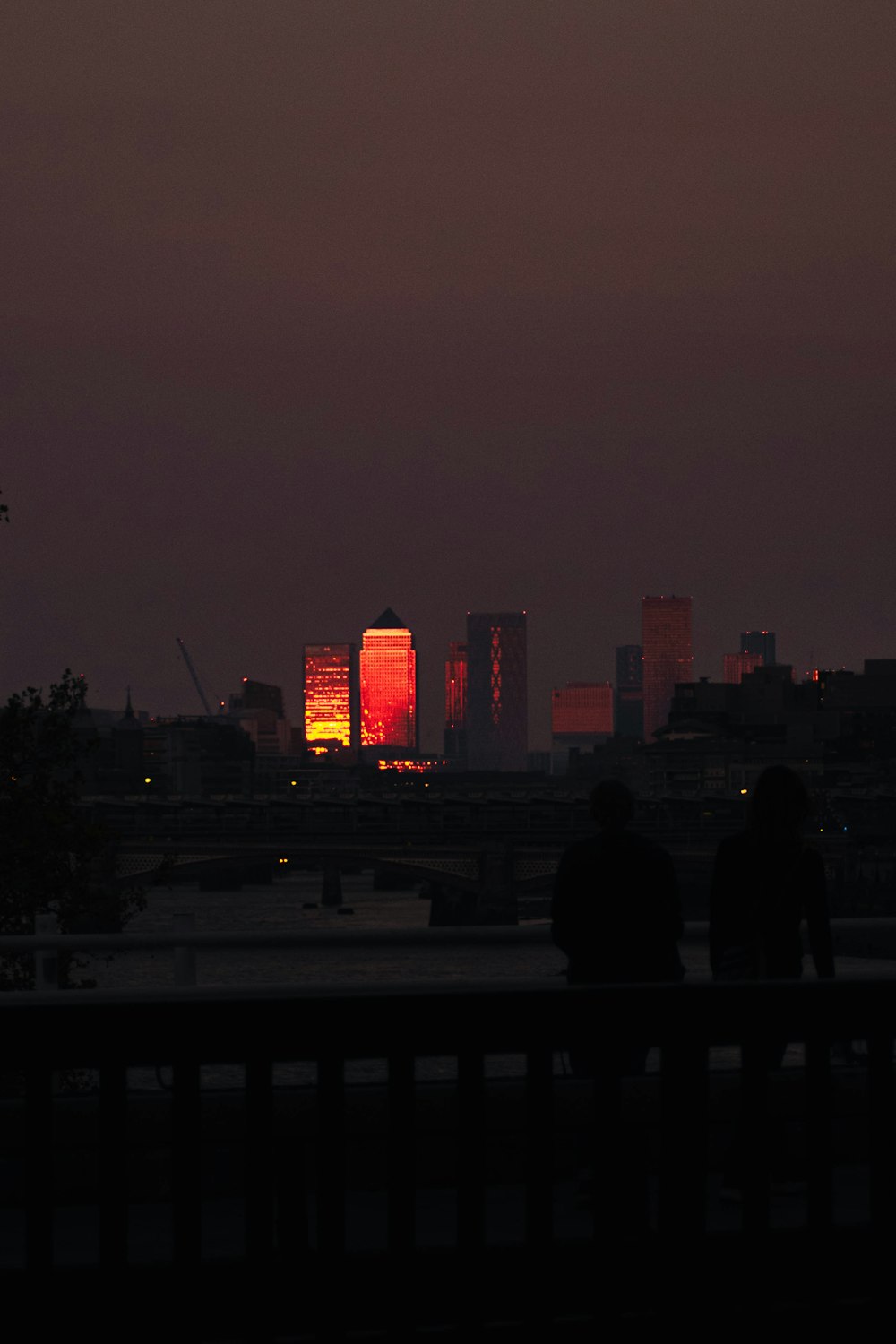 a couple people sitting on a bench in front of a city skyline