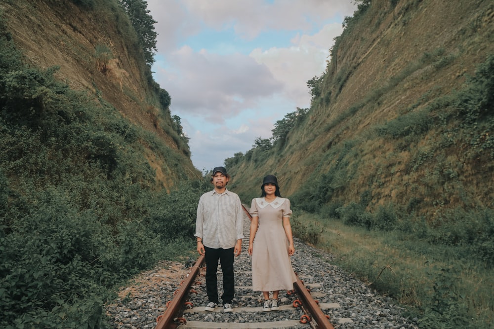 a man and woman standing on train tracks in the mountains