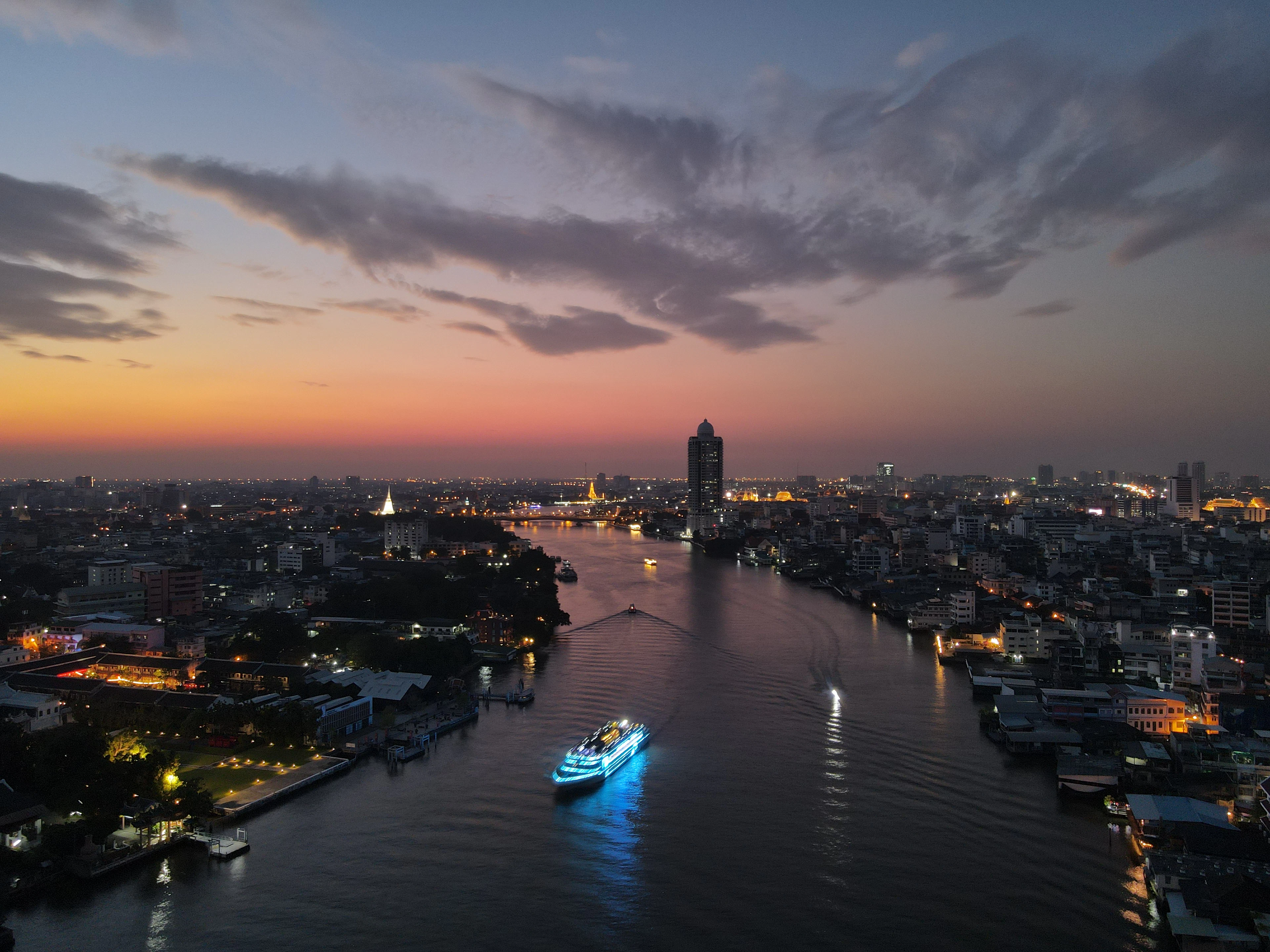 Dusk over the Chao Phraya River in Bangkok, with a lit dinner-cruise boat on the water