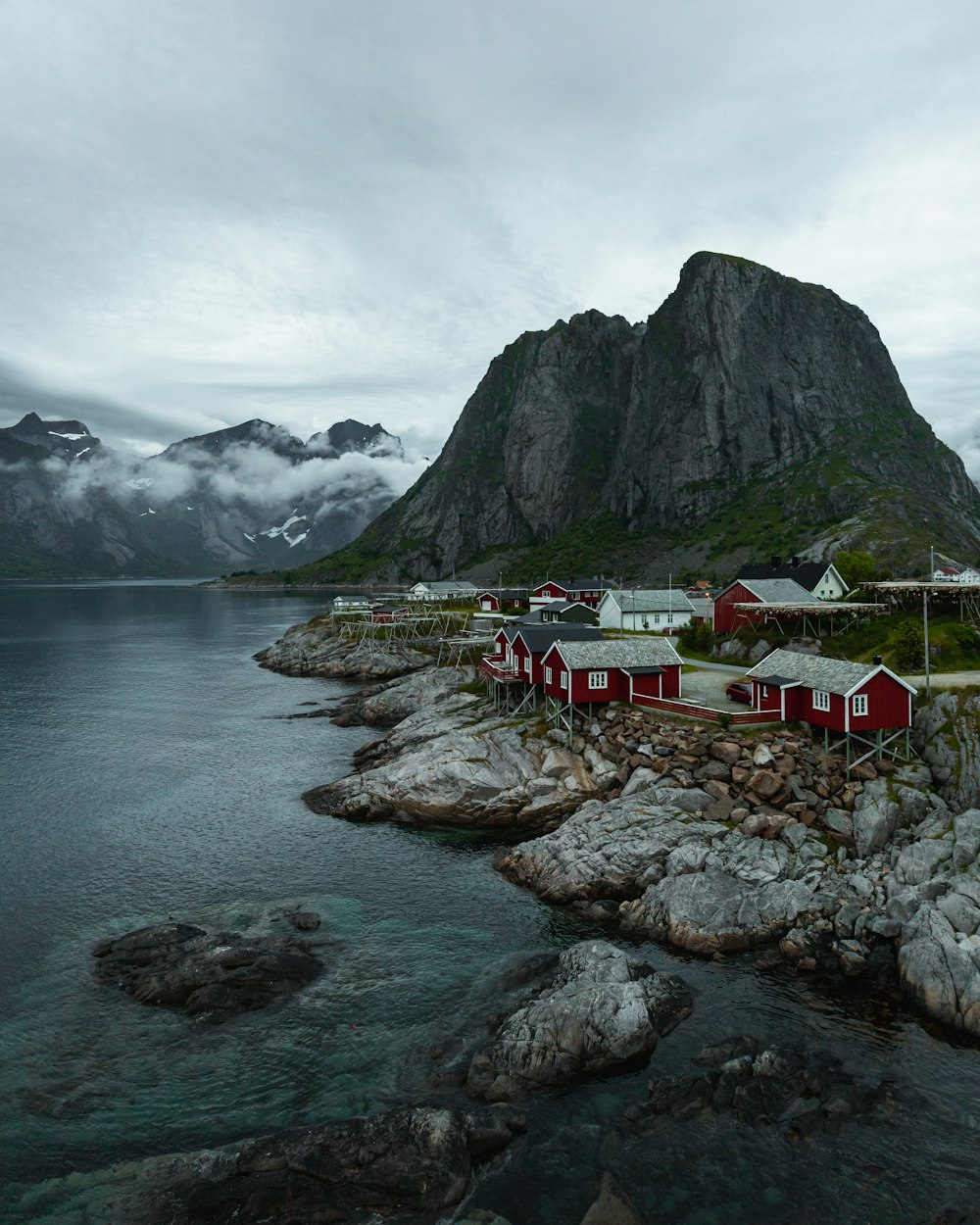 a group of houses by a body of water with mountains in the background