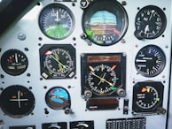 A collection of various analog gauges and dials from an aircraft instrument panel. The instruments include an airspeed indicator in knots, an altimeter, a vertical speed indicator, a compass, and an artificial horizon. Each gauge has distinct markings, needles, and some have colored flags.