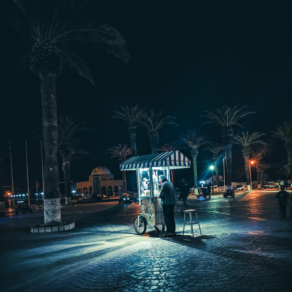 a person standing next to a small carousel in a plaza at night