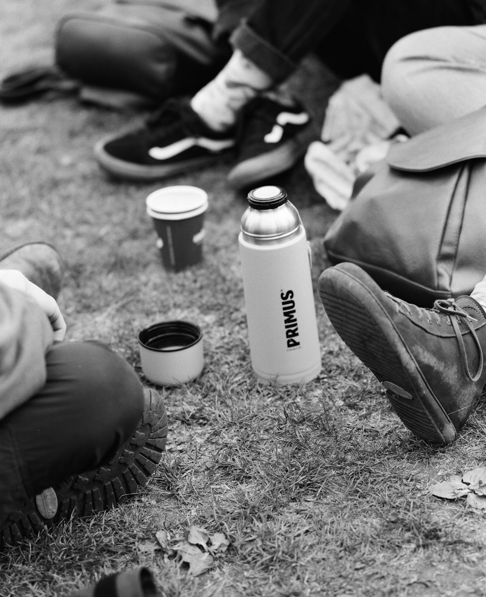 a group of people sitting on the grass with cups and a can