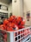 A collection of bright orange soccer balls with black patterns are piled inside a metal basket. The background is slightly blurred, showing part of a store interior with shelves.