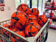 Rows of colorful sports balls lined up on a shelf in a retail store.