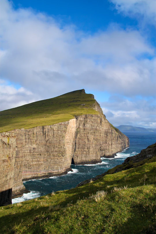 Nordic mountain lake under still dawn light in the Faroe Islands — cliffs, mist and grass-roof calm
