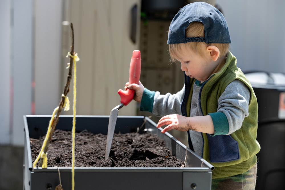 a young boy using a red tool to stir a substance in a container