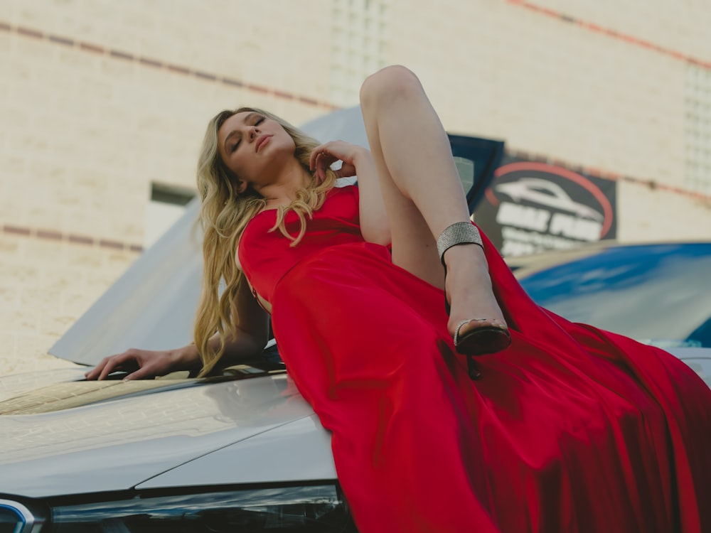 a woman in a red dress leaning on a car