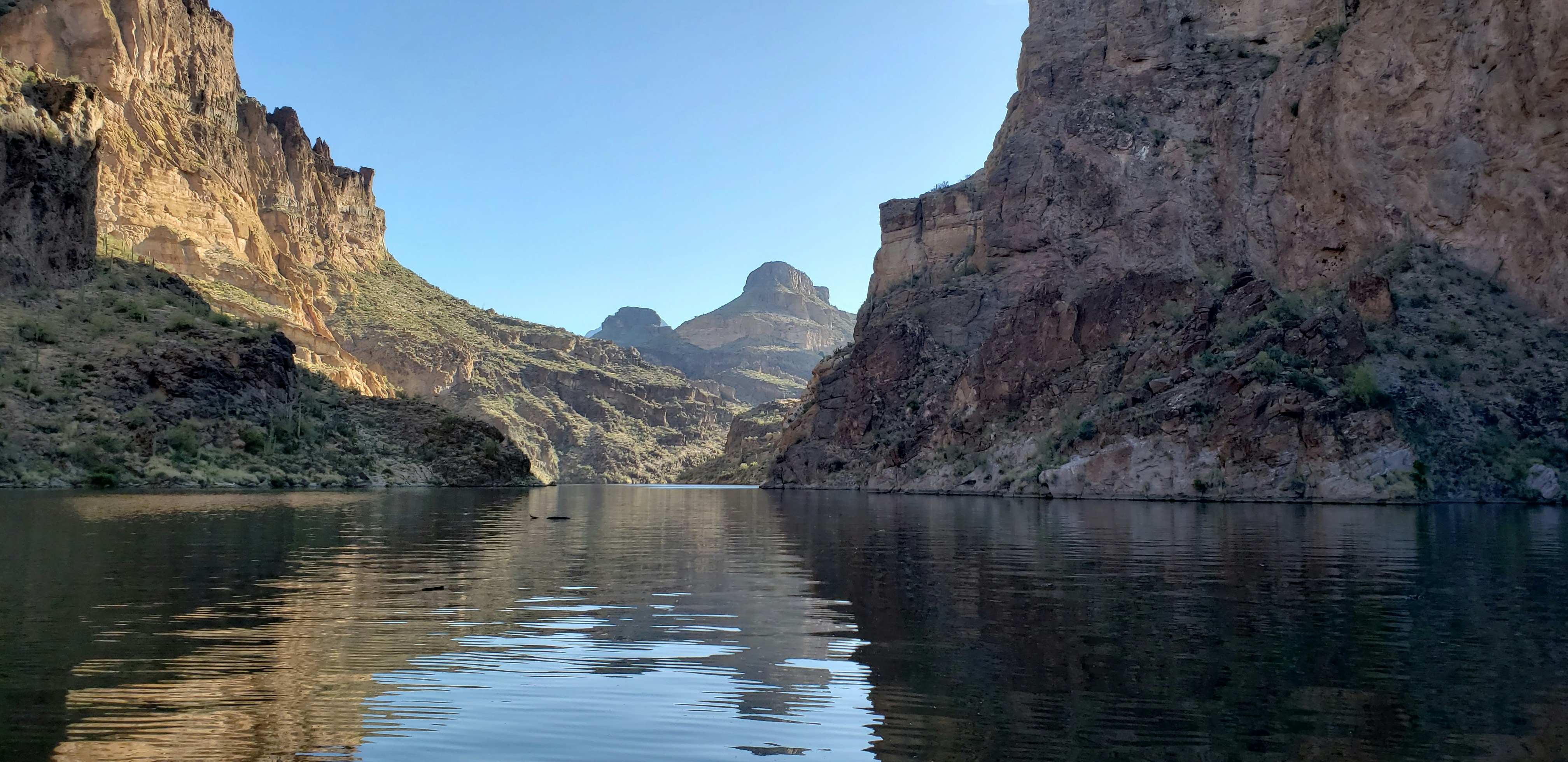 a body of water with a rocky cliff and trees on the side