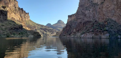 A serene mountain lake reflecting the clear blue sky surrounded by rocky cliffs