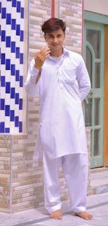 A smiling man dressed in a classic South Indian dhoti and kurta standing by a temple entrance.