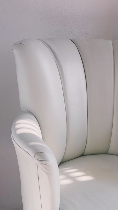 Close-up of a smooth, ivory silk shirt draped over a minimalist white chair in soft natural light.