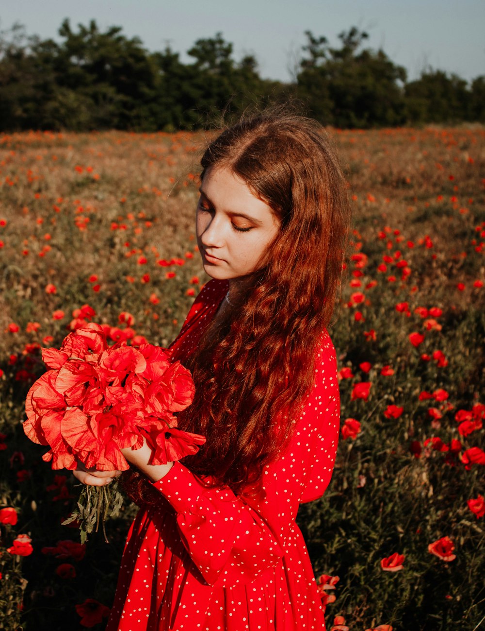 a person in a red dress holding a flower in a field of flowers