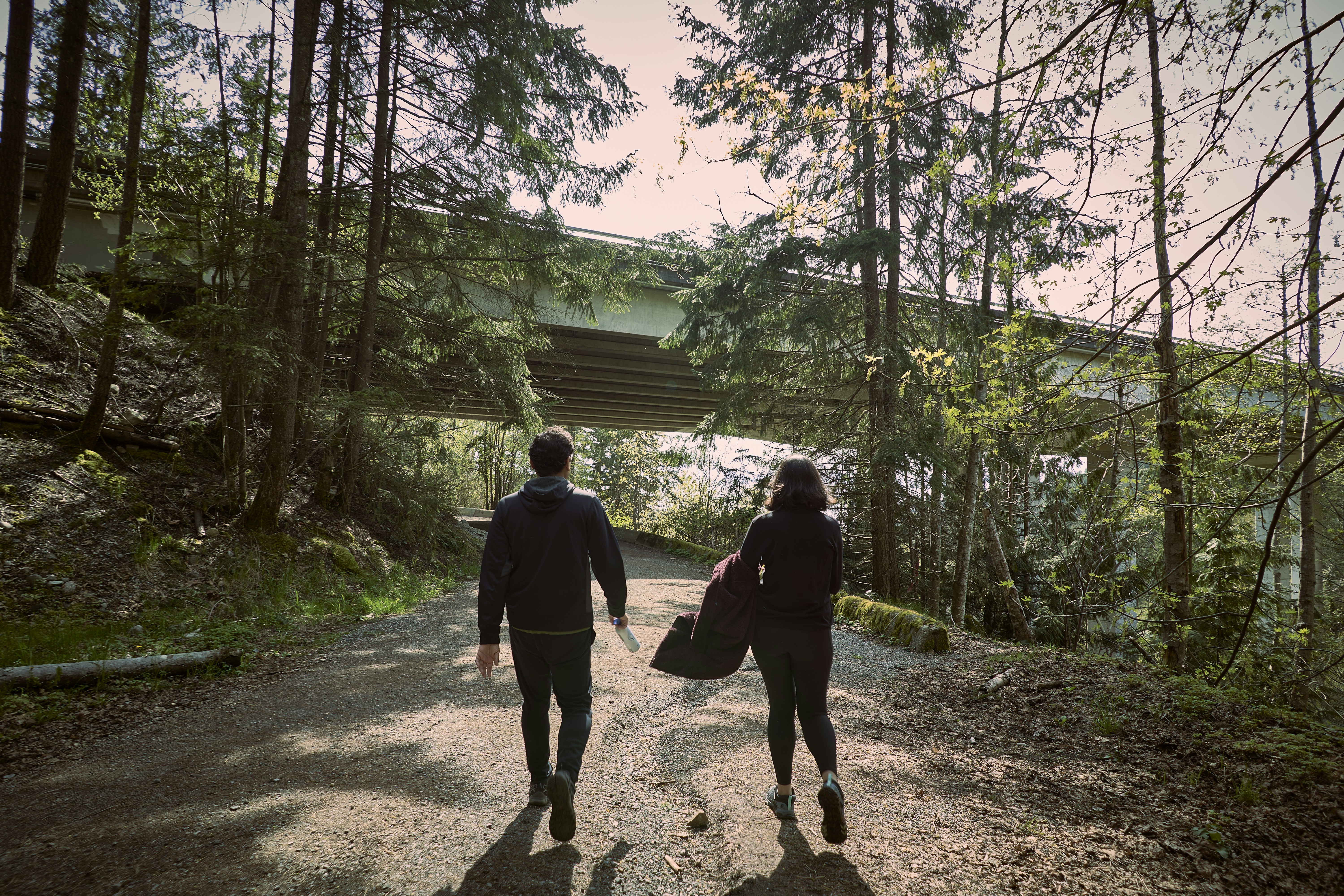 a man and woman walking on a dirt path in the woods