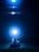 A small vehicle with wheels is positioned underwater, tethered to a glowing light source. The scene is bathed in a deep blue hue, creating an ethereal and mysterious ambiance.