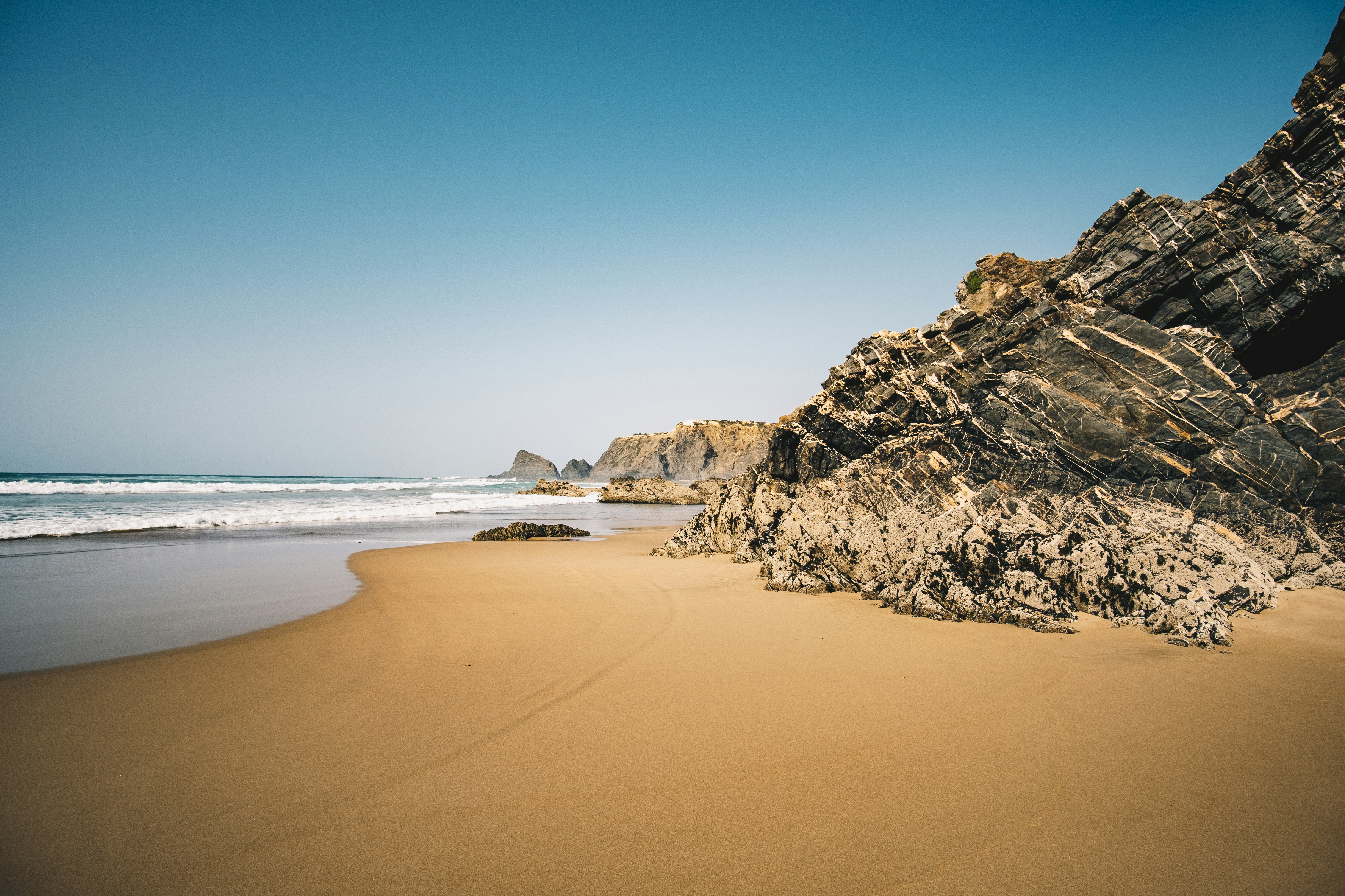 a sandy beach with a rocky cliff, 